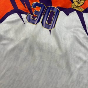 May include: A vintage soccer jersey with a white base, featuring orange and purple accents. The number "30" is prominently displayed in blue with a gold outline. The jersey includes the Umbro logo and a Scottish Football Association emblem.