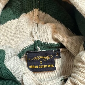 Pu&ograve; includere: Felpa con cappuccio in maglia color crema con strisce verdi. Il cappuccio e la parte superiore del petto presentano strisce verdi e crema alternate. L'etichetta recita "Ed Hardy X Urban Outfitters" e la taglia &egrave; "S".