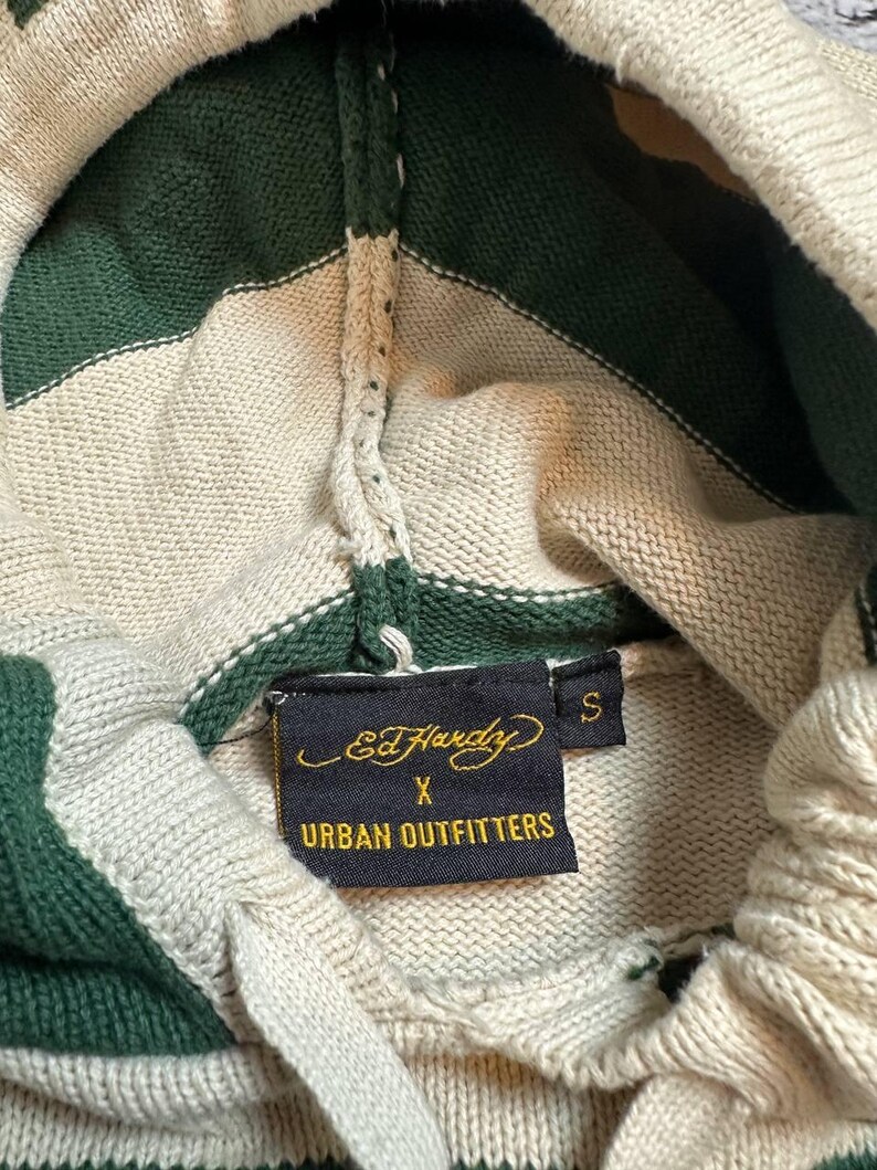 Pu&ograve; includere: Felpa con cappuccio in maglia color crema con strisce verdi. Il cappuccio e la parte superiore del petto presentano strisce verdi e crema alternate. L'etichetta recita "Ed Hardy X Urban Outfitters" e la taglia &egrave; "S".