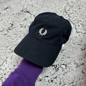 Könnte beinhalten: Marineblaue Baseballkappe mit gebogenem Schirm. Die Kappe hat ein weißes, gesticktes Lorbeerkranz-Logo. Hergestellt aus einem weichen Material, möglicherweise Nylon.