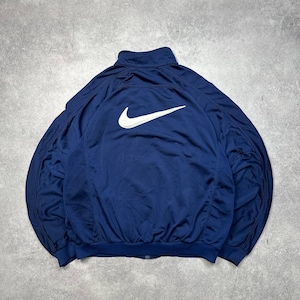 Pode incluir: Casaco de treino azul marinho com o log&oacute;tipo branco da Nike nas costas. O casaco tem fecho de correr completo e gola alta. O tecido &eacute; leve, possivelmente nylon.