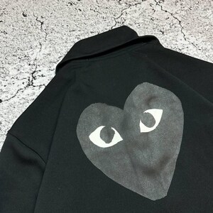 May include: Black sweatshirt featuring a large heart-shaped graphic with white eyes on the back. The sweatshirt has a collar and is made of a soft material. The graphic is centered on the back of the garment.