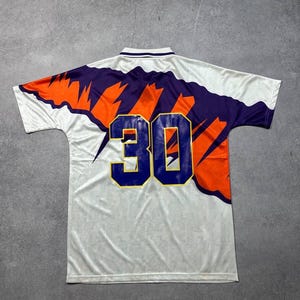 May include: White athletic jersey with a purple and orange design across the shoulders and back. The number "30" is prominently displayed on the back in blue with a gold outline. The jersey has a collared neckline.