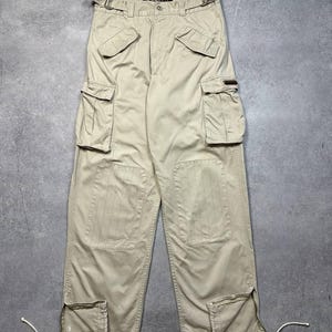 May include: Tan cargo pants with multiple pockets and a belt. The pants have a relaxed fit and feature a drawstring at the ankles. The pants are made of a durable fabric and are suitable for casual wear.