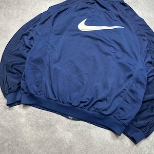 Pode incluir: Casaco desportivo azul marinho com o log&oacute;tipo Nike branco nas costas. O casaco tem fecho de correr completo, punhos canelados e bainha canelada. O casaco &eacute; feito de um material leve e respir&aacute;vel.