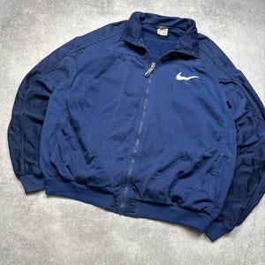 Pode incluir: Casaco azul marinho com z&iacute;per e logotipo branco da Nike no peito. O casaco tem gola, punhos e bainha canelados. O casaco &eacute; feito de um material leve.