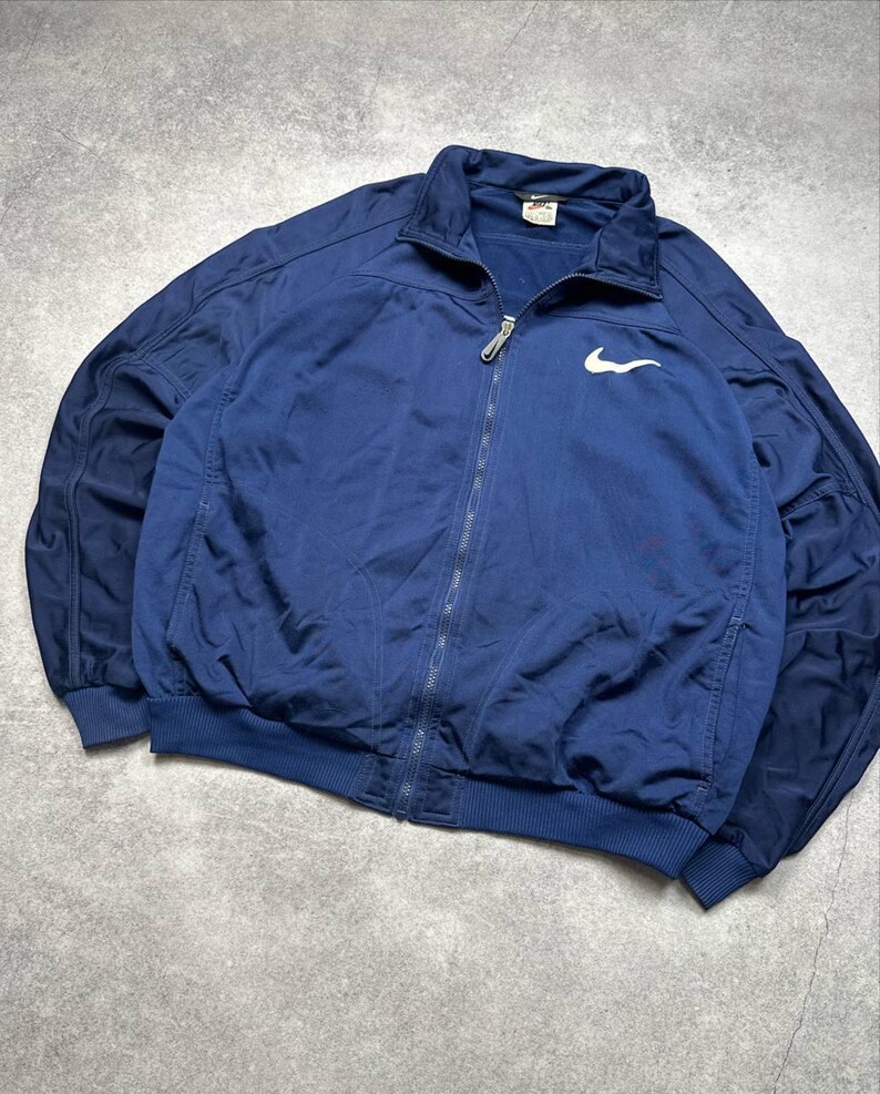 Pode incluir: Casaco azul marinho com z&iacute;per e logotipo branco da Nike no peito. O casaco tem gola, punhos e bainha canelados. O casaco &eacute; feito de um material leve.