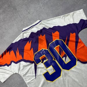 May include: White jersey with orange and purple accents, featuring the number 30 in blue. The jersey has a V-neck collar and a patterned design on the front and back. The jersey is made of a lightweight, breathable material.