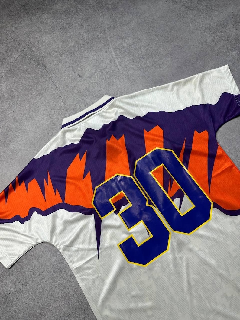 May include: White jersey with orange and purple accents, featuring the number 30 in blue. The jersey has a V-neck collar and a patterned design on the front and back. The jersey is made of a lightweight, breathable material.