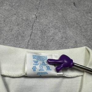 May include: Close-up of a white garment tag with care instructions. The tag includes symbols for washing, drying, and ironing. A purple hand-shaped pointer is touching the tag.