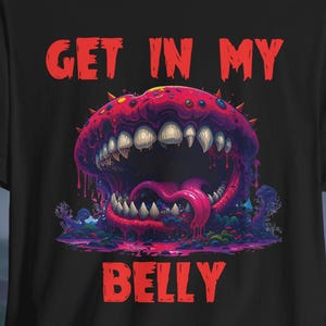 May include: Black t-shirt featuring a colorful monster graphic with the text "GET IN MY BELLY" in red. The monster has a large mouth with sharp teeth and a long tongue. The design is set against a dark, forest-like background.