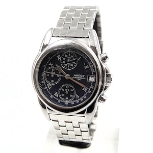 Puede incluir: Un reloj cronógrafo Ascot plateado con esfera azul oscuro, números romanos y múltiples subesferas. El reloj tiene una correa de acero inoxidable y una pantalla de fecha a las 3 en punto.