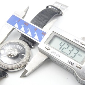 Puede incluir: Un reloj de pulsera Versus Versace con esfera negra, emblema de cabeza de le&oacute;n plateado y bisel plateado texturizado. Un calibre digital mide la caja del reloj en 42,33 mm. El reloj cuenta con una correa negra texturizada e &iacute;ndices plateados.