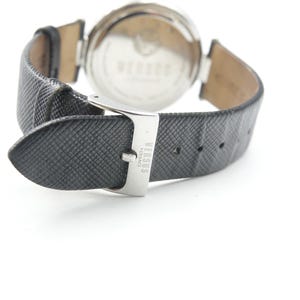 Puede incluir: Un reloj de pulsera con correa de cuero negro texturizado y hebilla de metal plateado. La hebilla tiene grabado el texto VERSUS VERSACE. La parte posterior de la caja del reloj es circular, met&aacute;lica y muestra el nombre VERSUS VERSACE.