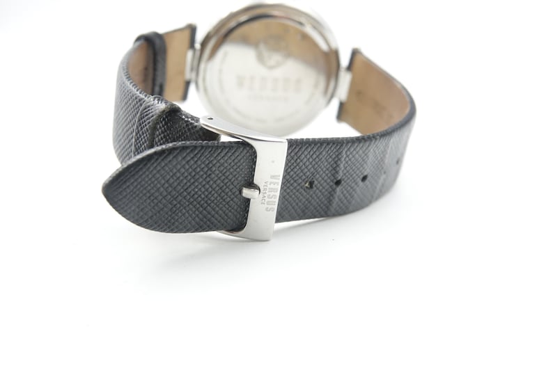 Puede incluir: Un reloj de pulsera con correa de cuero negro texturizado y hebilla de metal plateado. La hebilla tiene grabado el texto VERSUS VERSACE. La parte posterior de la caja del reloj es circular, met&aacute;lica y muestra el nombre VERSUS VERSACE.
