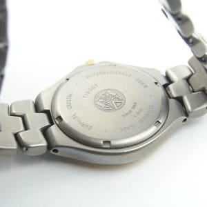 May include: Back view of a silver Tissot watch with a titanium case and sapphire crystal. The watch is water resistant to 100 meters and has a date window.