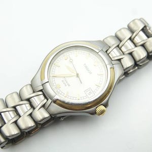 May include: A silver and gold Tissot watch with a white face and a stainless steel band.