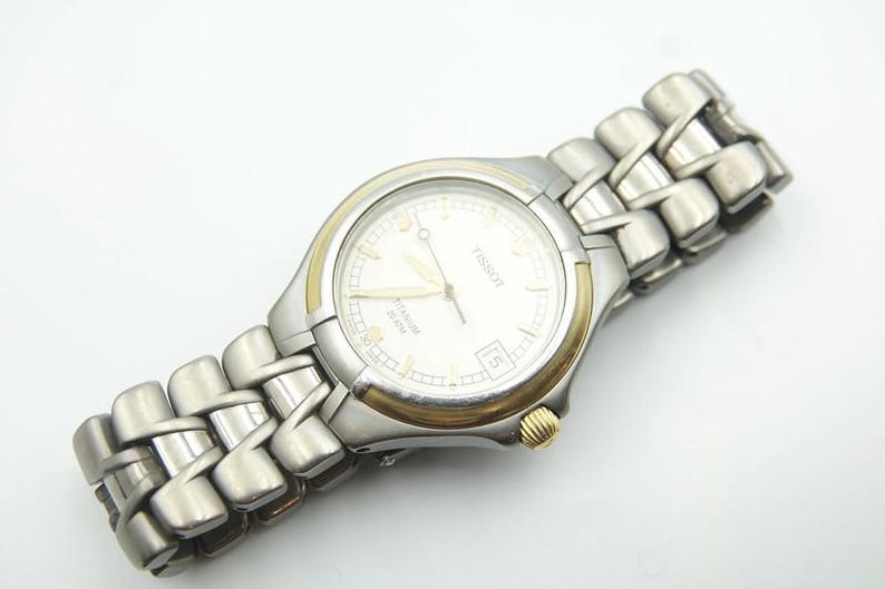 May include: A silver and gold Tissot watch with a white face and a stainless steel band.