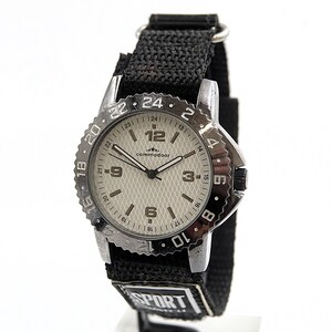May include: A silver-toned wristwatch with a black fabric band. The watch face is light gray with black numerals and hands. The bezel has a textured edge with numbers. The band has the word "SPORT" printed on it.