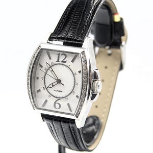 May include: A silver-toned rectangular watch with a white face, black hands, and a black leather band. The watch face features the number 12 and 6 in black, with small diamond accents around the bezel. The watch is branded with the name "HILFIGER".