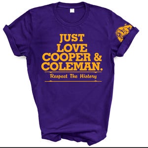 May include: A purple t-shirt with the text "JUST LOVE COOPER & COLEMAN. Respect The History" in gold lettering. A gold graphic is on the sleeve. The shirt is folded.