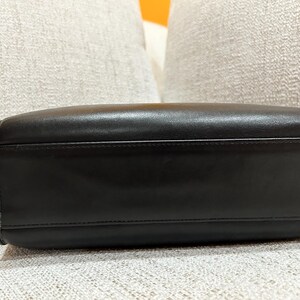 May include: A black leather handbag with a rectangular shape. The bag has a handle on one side and a smooth, shiny surface. The stitching is visible along the edges, and the bag appears to be well-constructed.