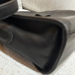 May include: Close-up of a black leather handbag with a shoulder strap. The bag has a rectangular shape with rounded corners and a subtle buckle detail on the top. The leather appears smooth and glossy.