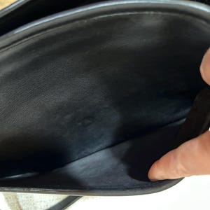 May include: Black leather handbag with a flap closure. The interior of the bag is visible, showing a spacious compartment and a smaller pocket. The bag appears to be well-maintained and in good condition.