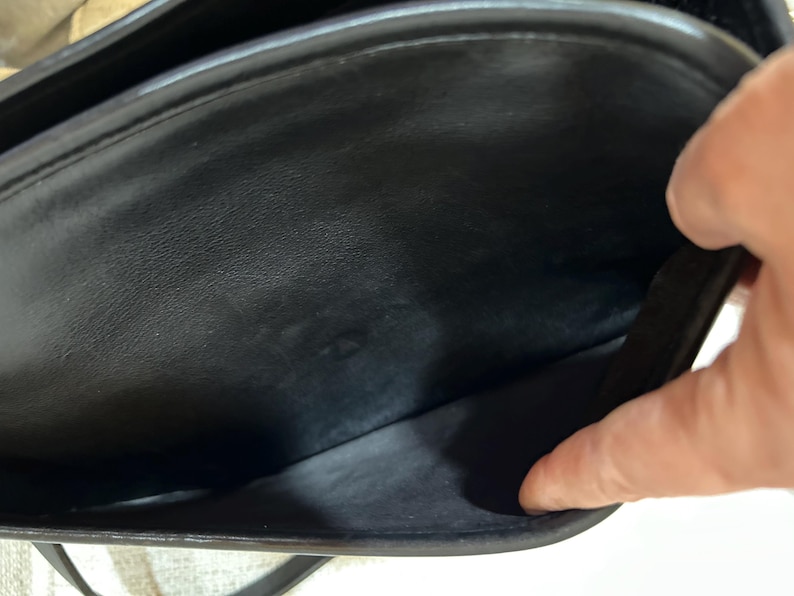 May include: Black leather handbag with a flap closure. The interior of the bag is visible, showing a spacious compartment and a smaller pocket. The bag appears to be well-maintained and in good condition.