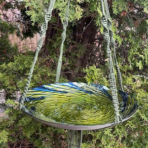 Può includere: Un bagno per uccelli in vetro verde con un motivo a spirale appeso a un cordoncino in macramé.