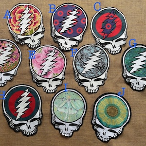 Peut inclure: Une collection de dix écussons en forme de crâne, chacun avec un design unique à l'intérieur de la tête du crâne. Les motifs comprennent des motifs floraux, des formes géométriques et un éclair. Les écussons sont bordés de noir.