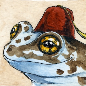 May include: A watercolor painting of a frog wearing a red fez with a yellow tassel. The frog has brown and white spots on its blue skin. The frog's eyes are large and yellow with black pupils.