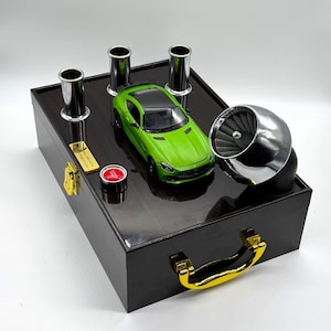 May include: A black wooden box with a gold handle, featuring a green toy car, four silver exhaust pipes, and a silver turbocharger. The box has a red button and a gold plaque with the text "Limited Edition".