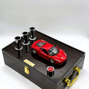 Puede incluir: Una caja de madera negra con una manija dorada y un coche de juguete rojo en su interior. La caja tiene una placa que dice "Ferrari 458 Italia Limited Edition".