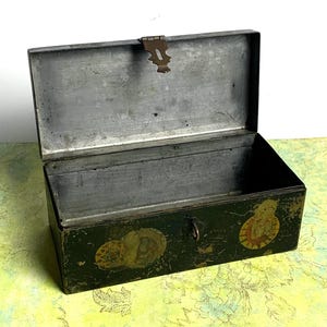 May include: An open, vintage green metal box with a hinged lid and a latch. The box has decorative circular decals on the front and sides. The interior is a silver-gray color, and the box shows signs of wear.