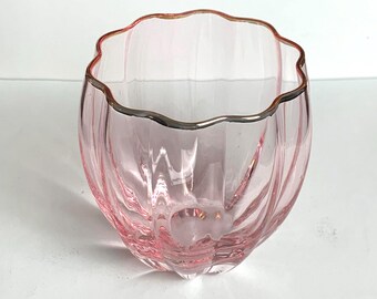 May include: A pink glass bowl with a wavy rim and a silver-colored trim. The bowl has vertical ridges and a rounded base. The glass is transparent, allowing light to pass through.