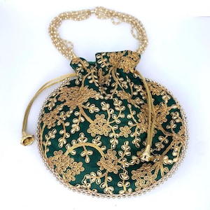 May include: A round, dark green drawstring bag with gold floral embroidery. The bag has a beaded handle and a gold drawstring closure. The edges are trimmed with small, silver-colored beads. The bag is likely used for carrying small items.
