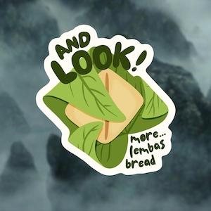 May include: A sticker featuring a cartoon illustration of lembas bread wrapped in green leaves. The text "AND LOOK!" is at the top, with "more... lembas bread" at the bottom. The background is a blurred mountain scene.