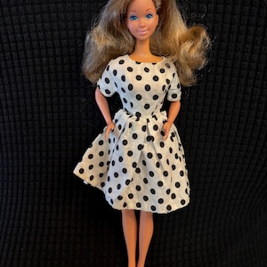 May include: A vintage doll with long brown hair, blue eyes, and a white dress with black polka dots.