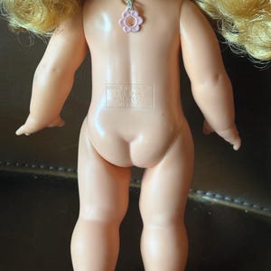 May include: Back view of a vintage doll with blonde hair. The doll has a light skin tone and is wearing a pink flower charm. The text on the doll reads "&copy;1967 Mattel Inc. U.S.A. For Pat. Pend. Mexico."