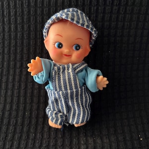 4” Kewpie Doll, Soft Rubber Vinyl. Movable Arms. Starfish hands. Wearing striped denim overalls and engineer cap and blue shirt. Cute!