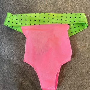 May include: Pink swimsuit with a green and black polka dot trim.
