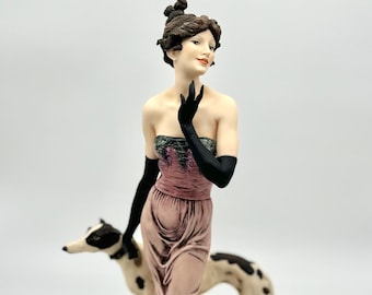 May include: A porcelain figurine of a woman in a pink gown with a black and white dog. The woman is wearing black gloves and has her hair up in a bun. The figurine is on a black base.
