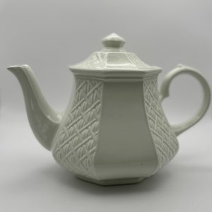 May include: White ceramic teapot with a woven pattern and a lid. The teapot has a spout and a handle.