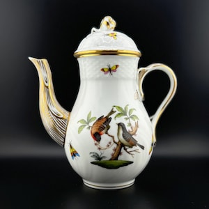 May include: White porcelain coffee pot with gold accents and a floral design featuring birds and butterflies. The pot has a round body and a spout with a gold trim.