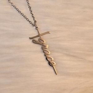 Pode incluir: Um colar de prata com um pingente de cruz que tem a palavra "Grace" escrita nele.