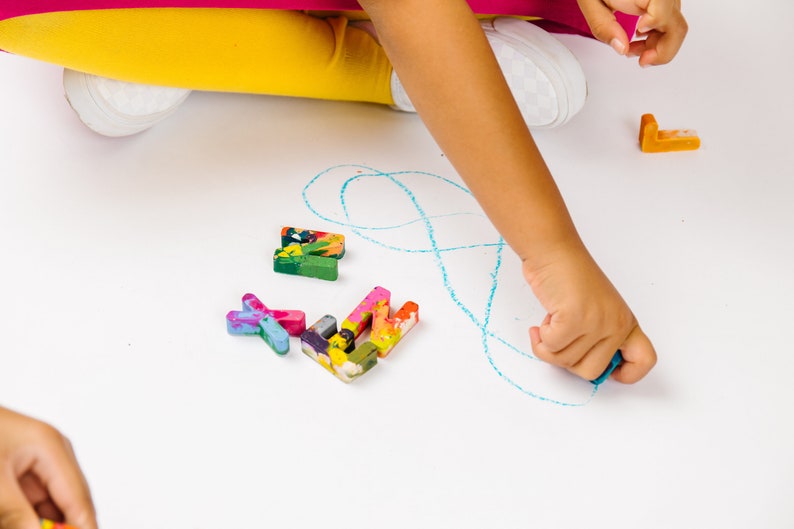 Image is of kids hands coloring with crayon letters. These custom crayons in the shape of rainbow crayon letters are a perfect holiday gift idea or stocking stuffer for children.