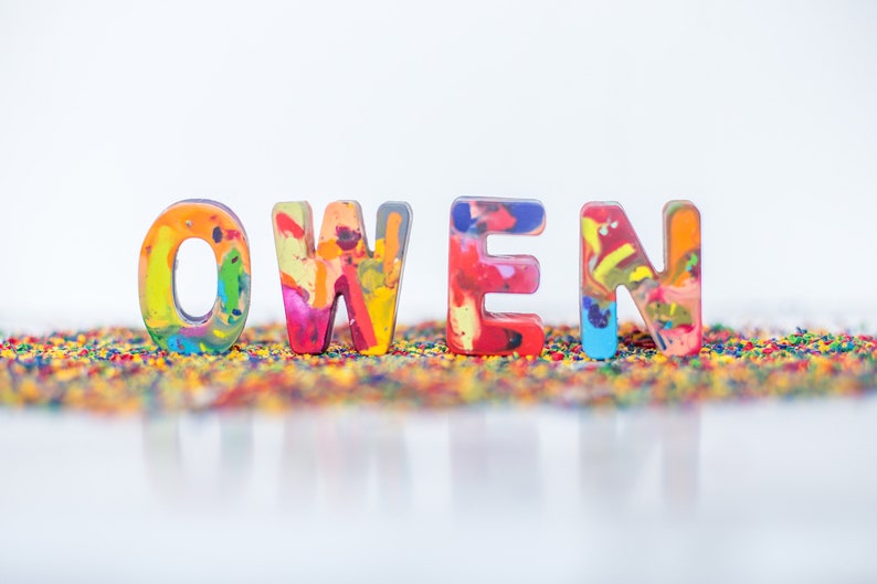 May include: The name "OWEN" spelled out in colorful, multi-colored crayon letters on a bed of rainbow-colored crayon shavings.