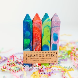 May include: Four colorful crayon sticks with a marbled design. The crayons are packaged together with a brown label that reads "Crayon Stix: The Original Rainbow Crayons - Made from Pure, Plant-Based Crayons".