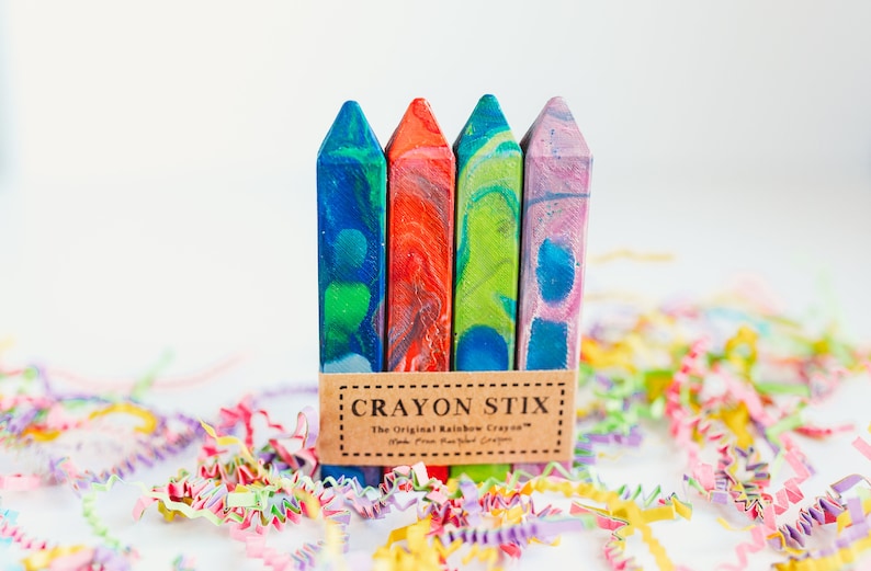 May include: Four colorful crayon sticks with a marbled design. The crayons are packaged together with a brown label that reads "Crayon Stix: The Original Rainbow Crayons - Made from Pure, Plant-Based Crayons".